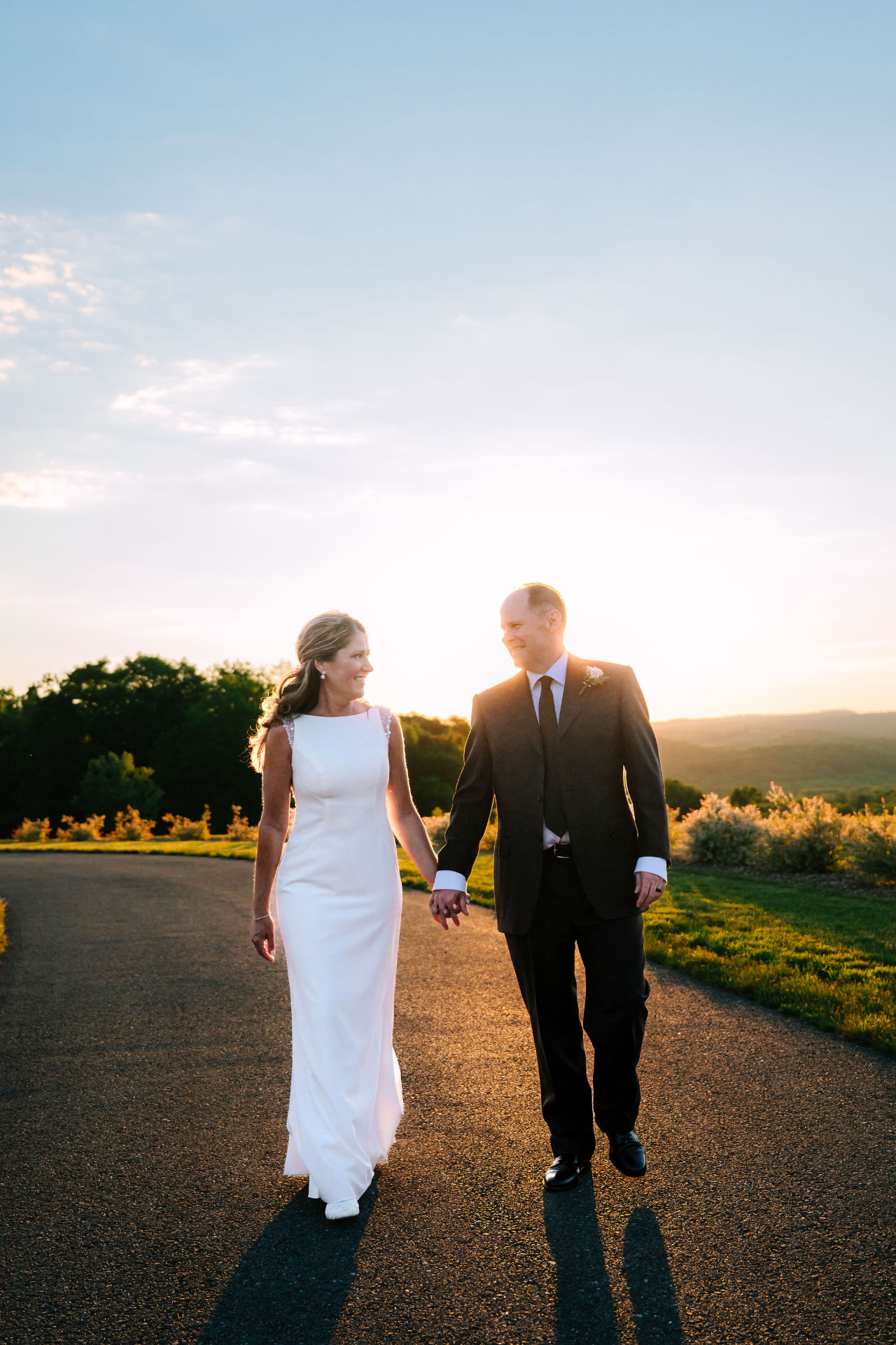 Greg and Sonnie walking hand in hand down a drive at sunset