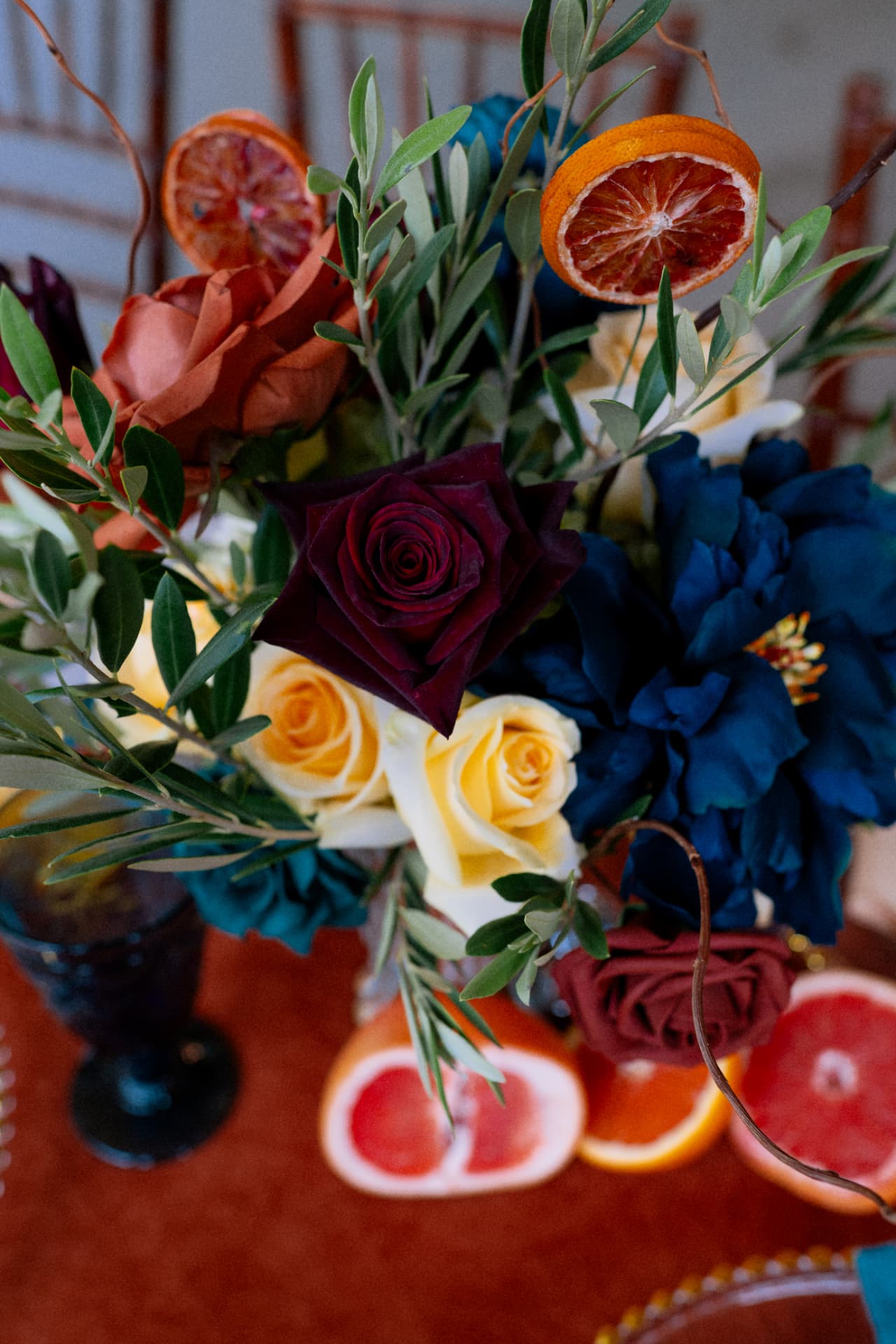 A centerpiece of deep red, yellow, and blue blooms with dried citrus