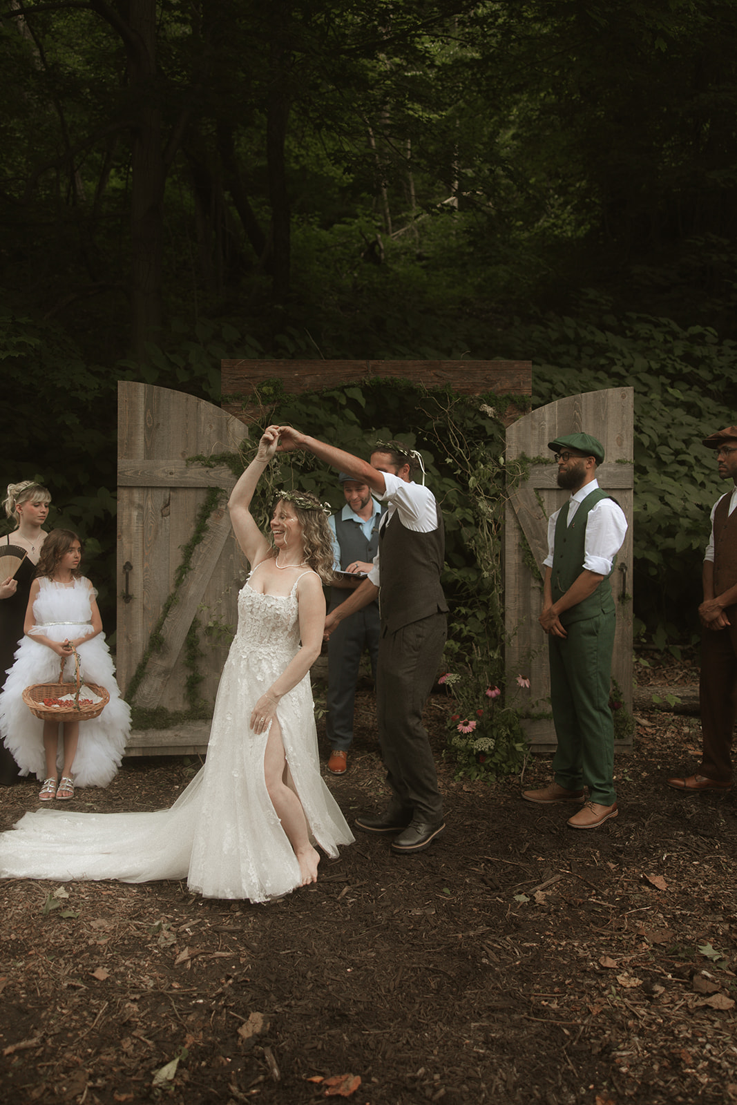 Dani spinning beneath a wooden arch in the woods with the wedding party nearby