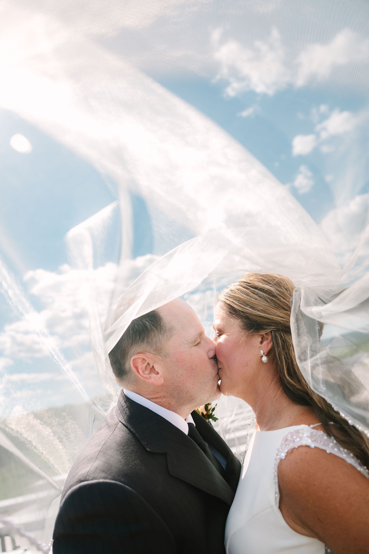 Greg and Sonnie kissing beneath a veil against a blue sky