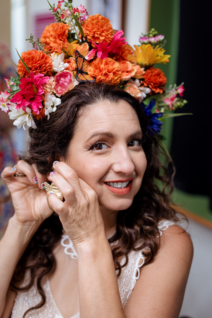 Alison adjusting an earring beneath a large colorful flower crown
