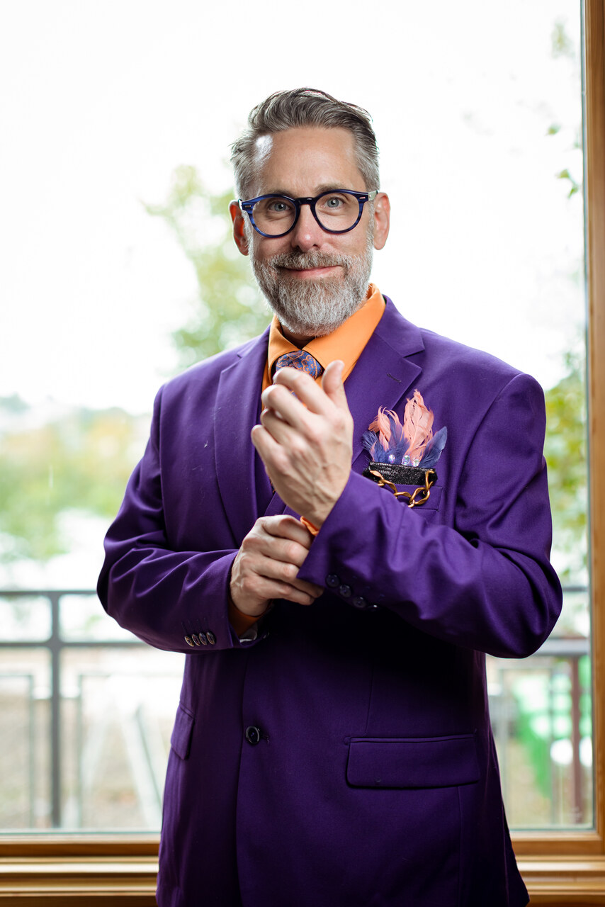 Benjamin smiling in a purple suit and feathered boutonniere