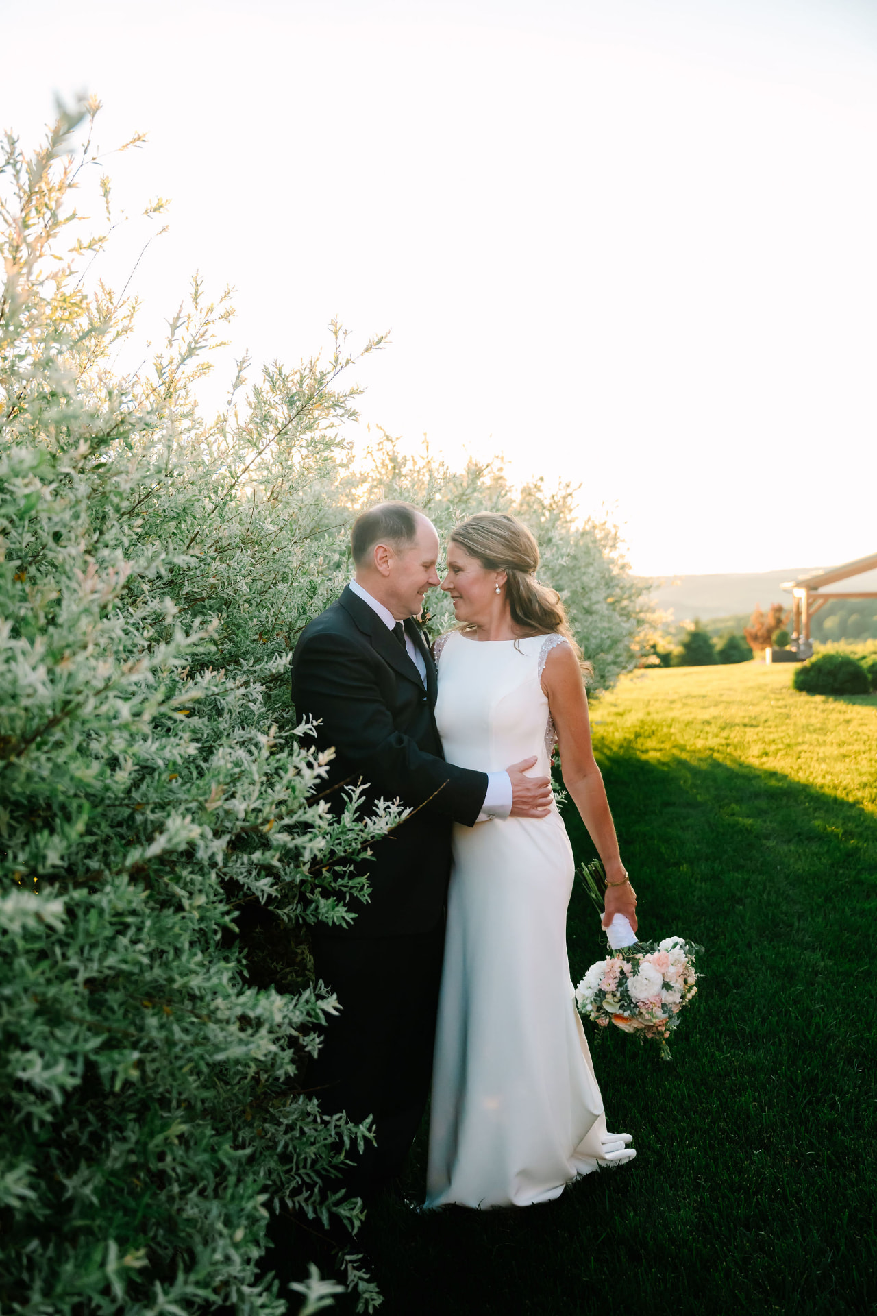 Greg and Sonnie forehead to forehead beside silvery shrubs at golden hour